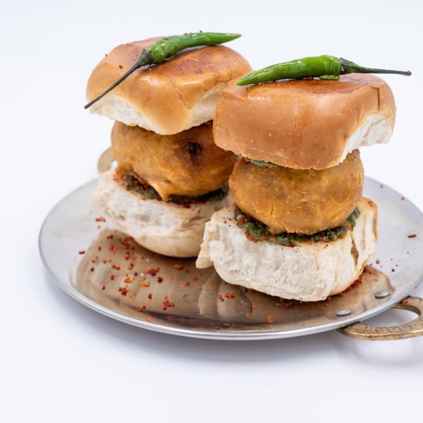 Two WOW TIKKA vada pavs with green chilies on top, served on a metal plate.