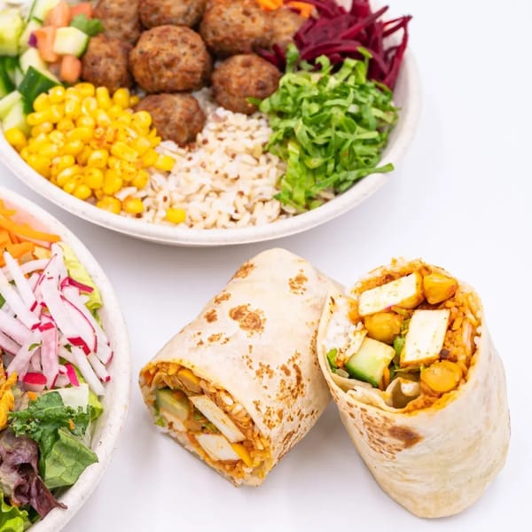 Two WOW TIKKA wraps filled with paneer, chickpeas, and rice, alongside a colorful salad bowl.