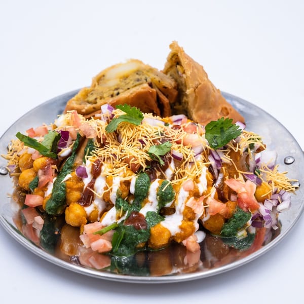 WOW TIKKA's Indian chaat with chickpeas, sauces, chopped vegetables, and crispy noodles, served with samosas.